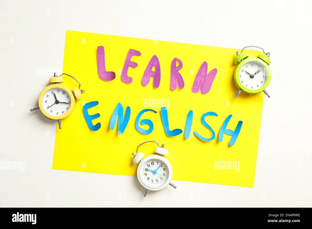 Note with phrase Learn English and alarm clocks on white background