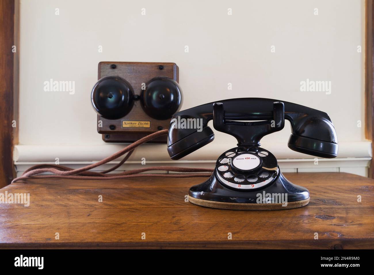 Close-up of fixed line black antique Northern Electric rotary dial telephone on wooden desk table in kitchen inside old 1892 Canadiana home. Stock Photo