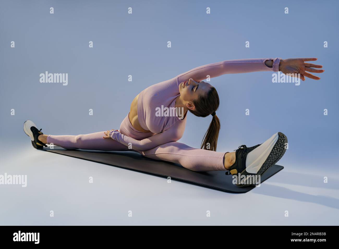 Flexible woman doing stretching exercises on yoga mat on studio ...
