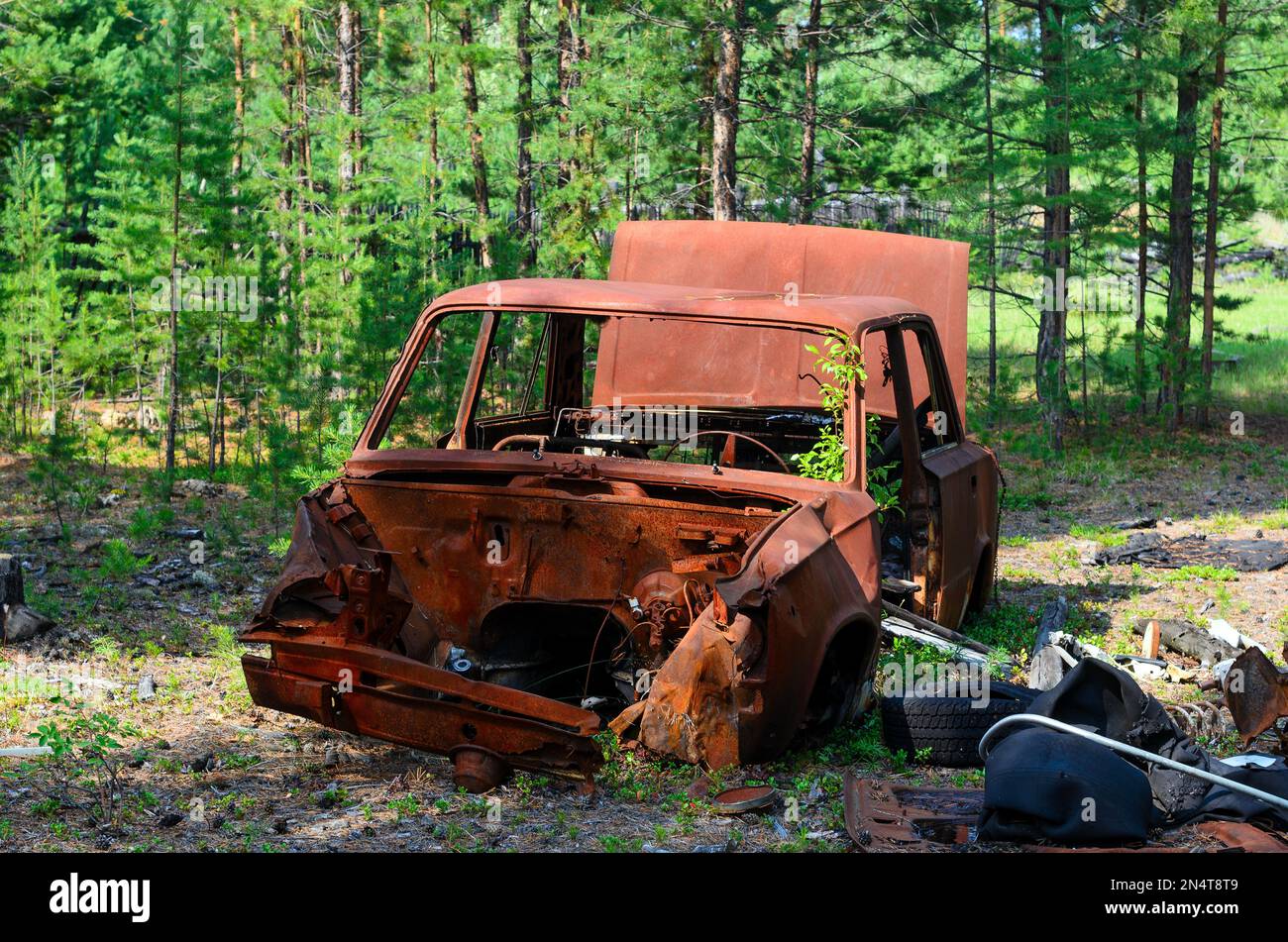 Iron rusty body of the Soviet car lies among the debris in the shade in ...