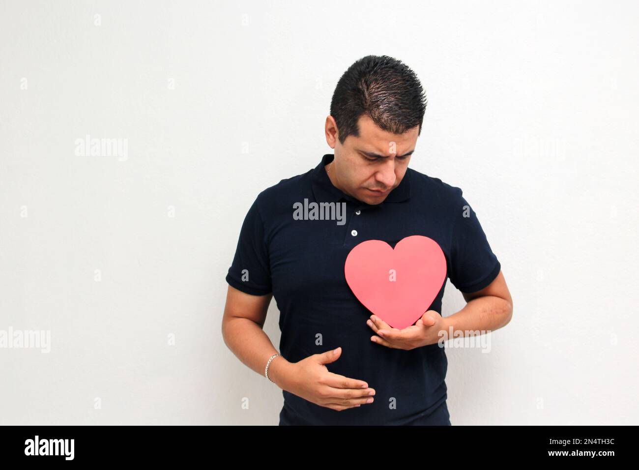 Latino adult man with a big red heart shows his anger, disgust, sadness ...