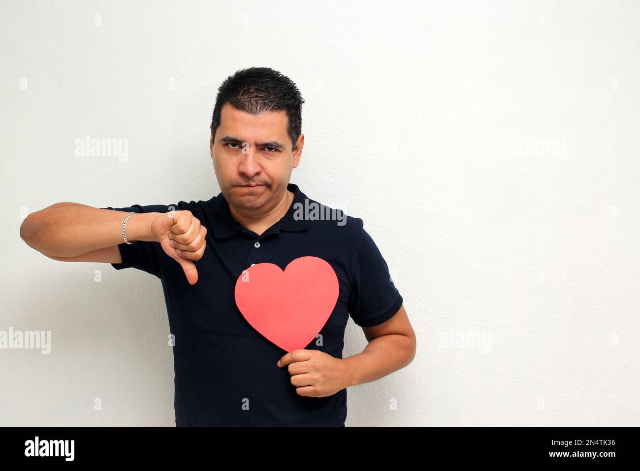 Latino adult man with a big red heart shows his anger, disgust, sadness ...