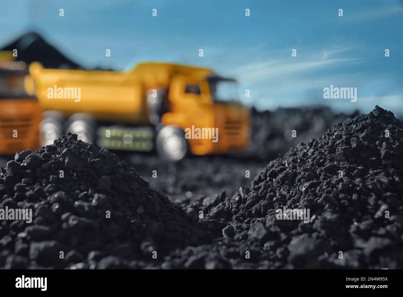 Pile of coal and blurred yellow truck on background, closeup Stock Photo