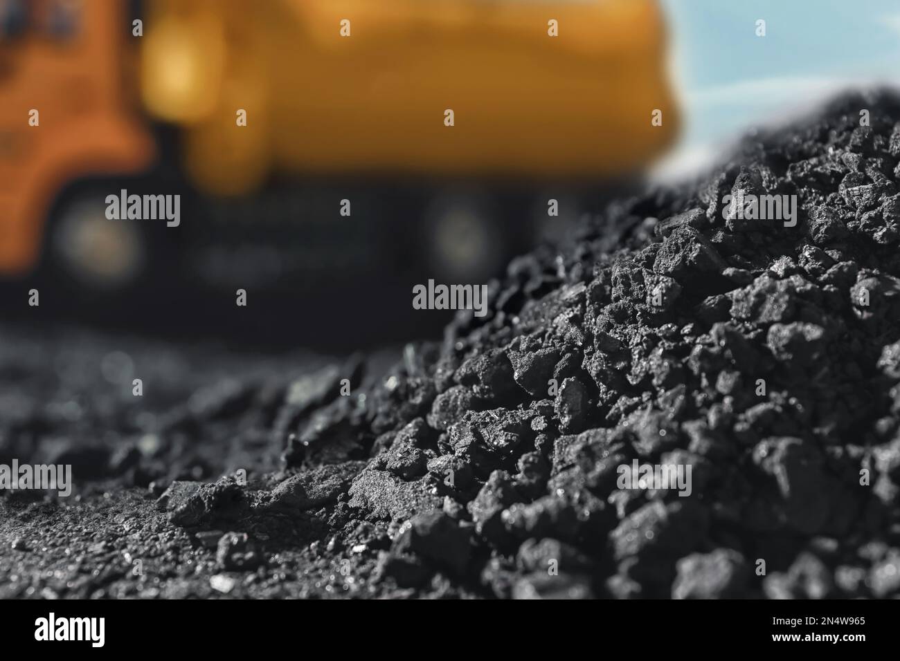 Pile of coal and blurred yellow truck on background, closeup Stock Photo