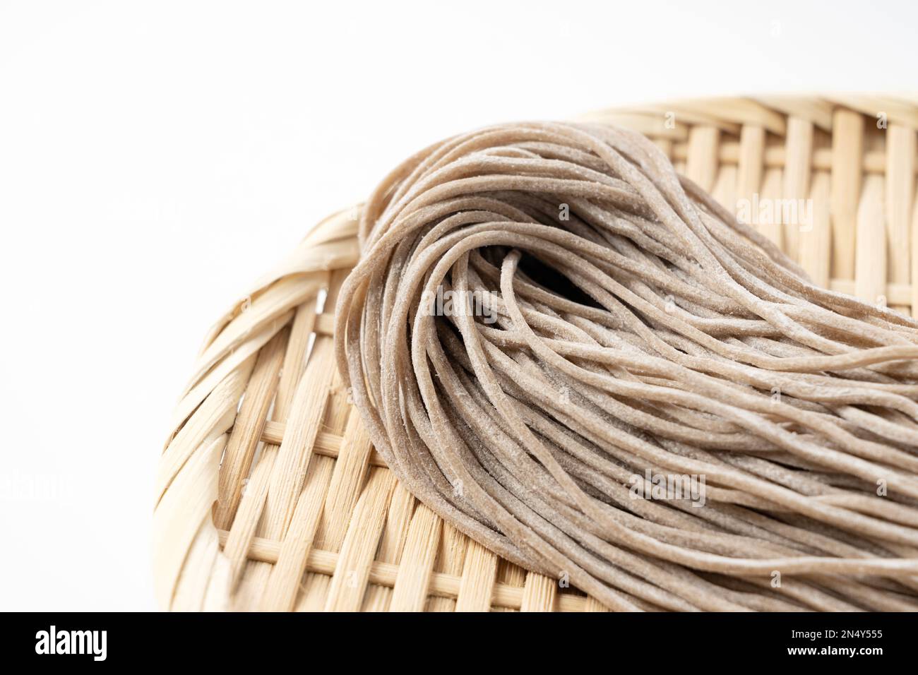 Raw soba noodles in a bamboo colander placed against a white background