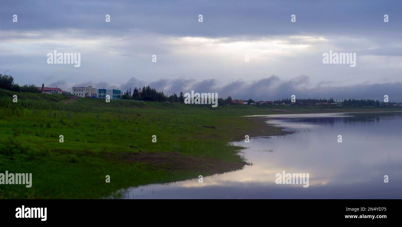 Strange monotonous fat clouds float in the distance in the evening sky at sunset over the river in the wild North of Yakutia vilyu ryados with the vil Stock Photo