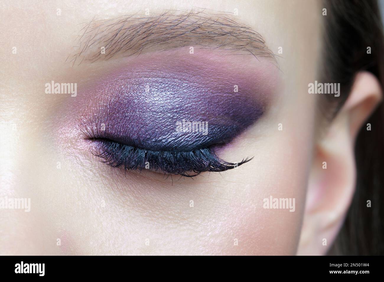 Closeup macro shot of closed human female eye. Woman with lilac beauty eyes makeup. Girl with perfect skin and purple smoky eyes eye shadows. Stock Photo