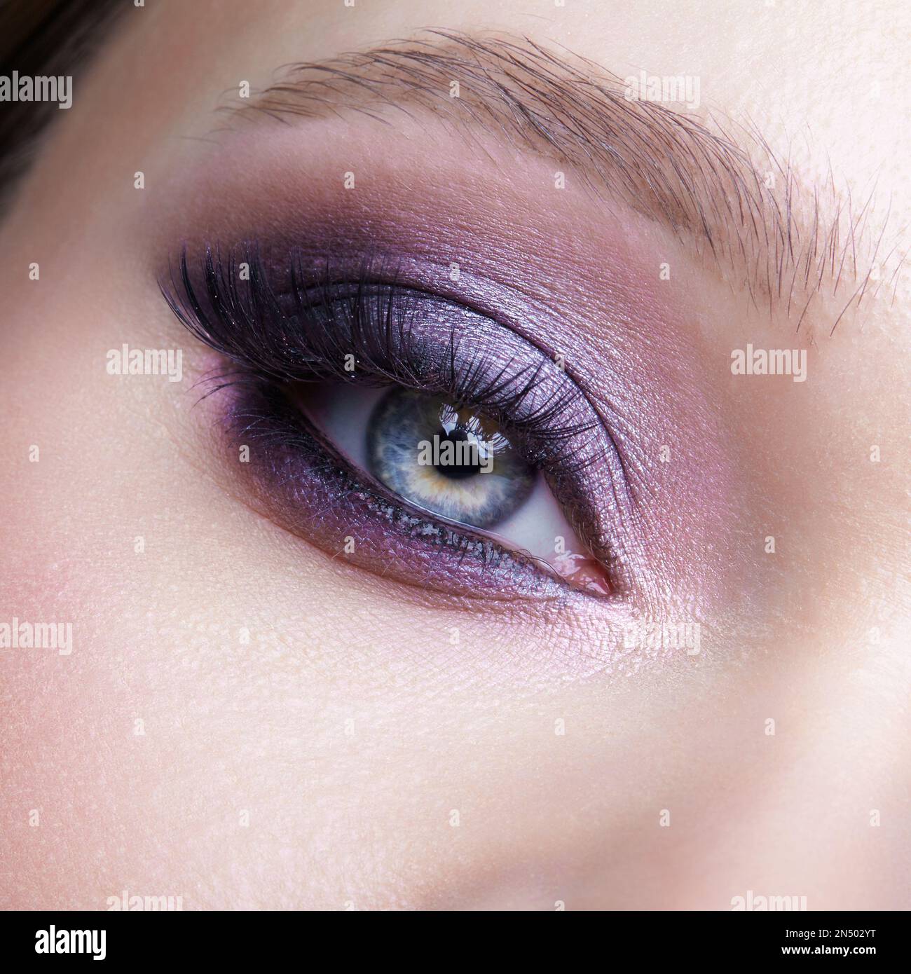 Closeup macro shot of human female eye. Woman with lilac beauty eyes makeup. Girl with perfect skin and purple smoky eyes eye shadows. Stock Photo