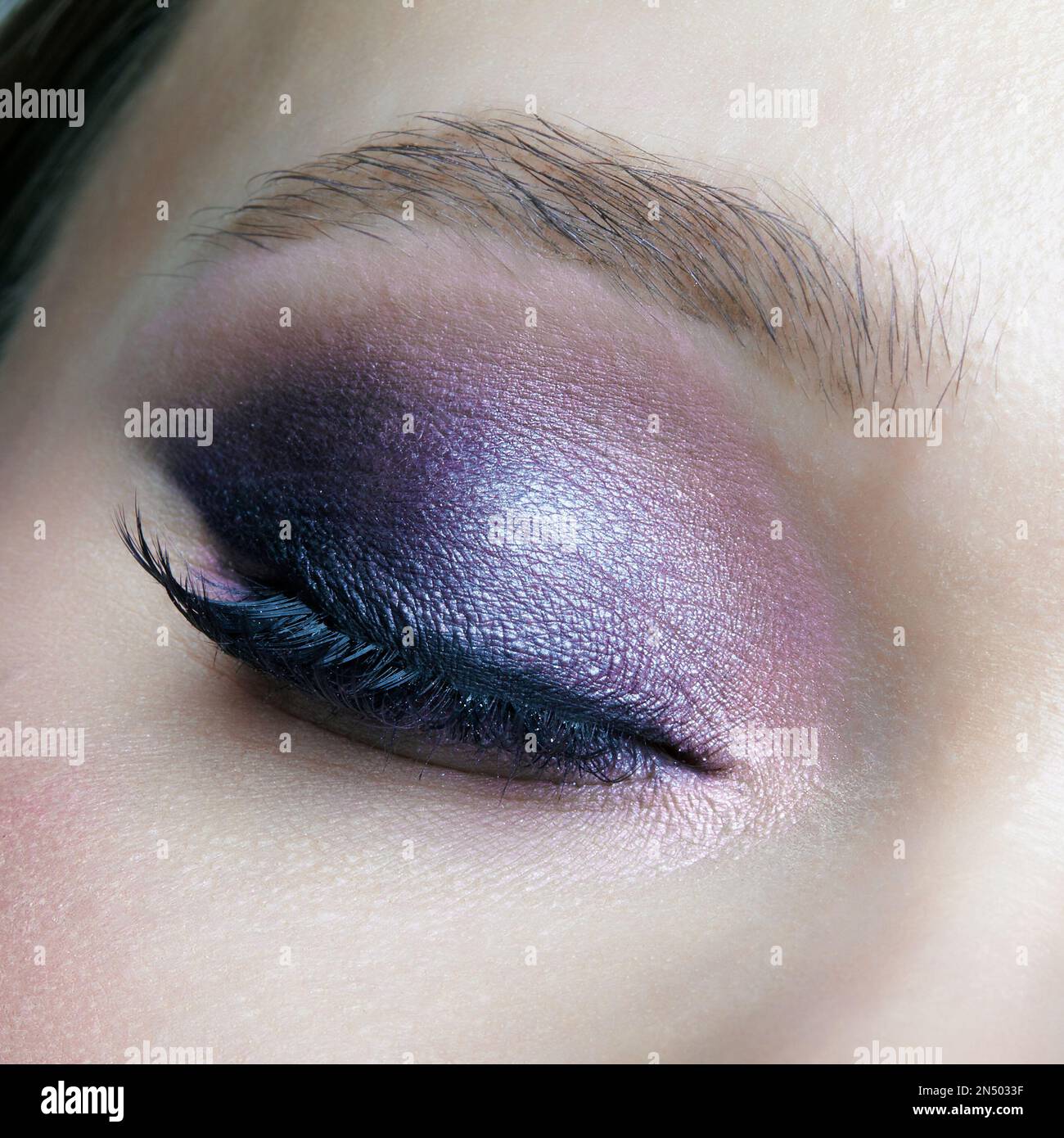 Closeup macro shot of closed human female eye. Woman with lilac beauty eyes makeup. Girl with perfect skin and purple smoky eyes eye shadows. Stock Photo