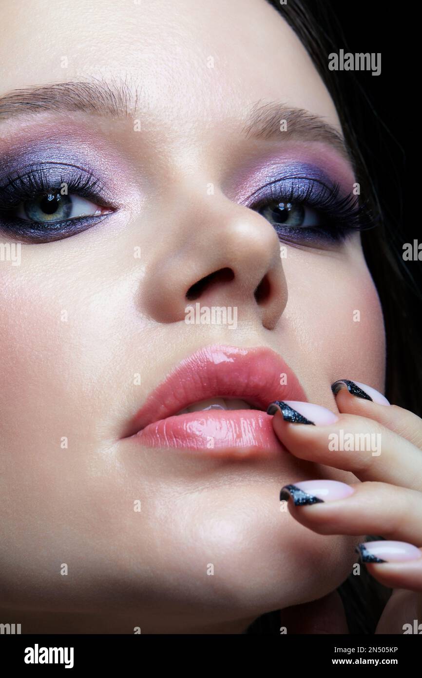 Portrait of young female face with hand near face. Woman with lilac beauty eyes makeup. Girl with perfect skin and purple smoky eyes eye shadows. Stock Photo