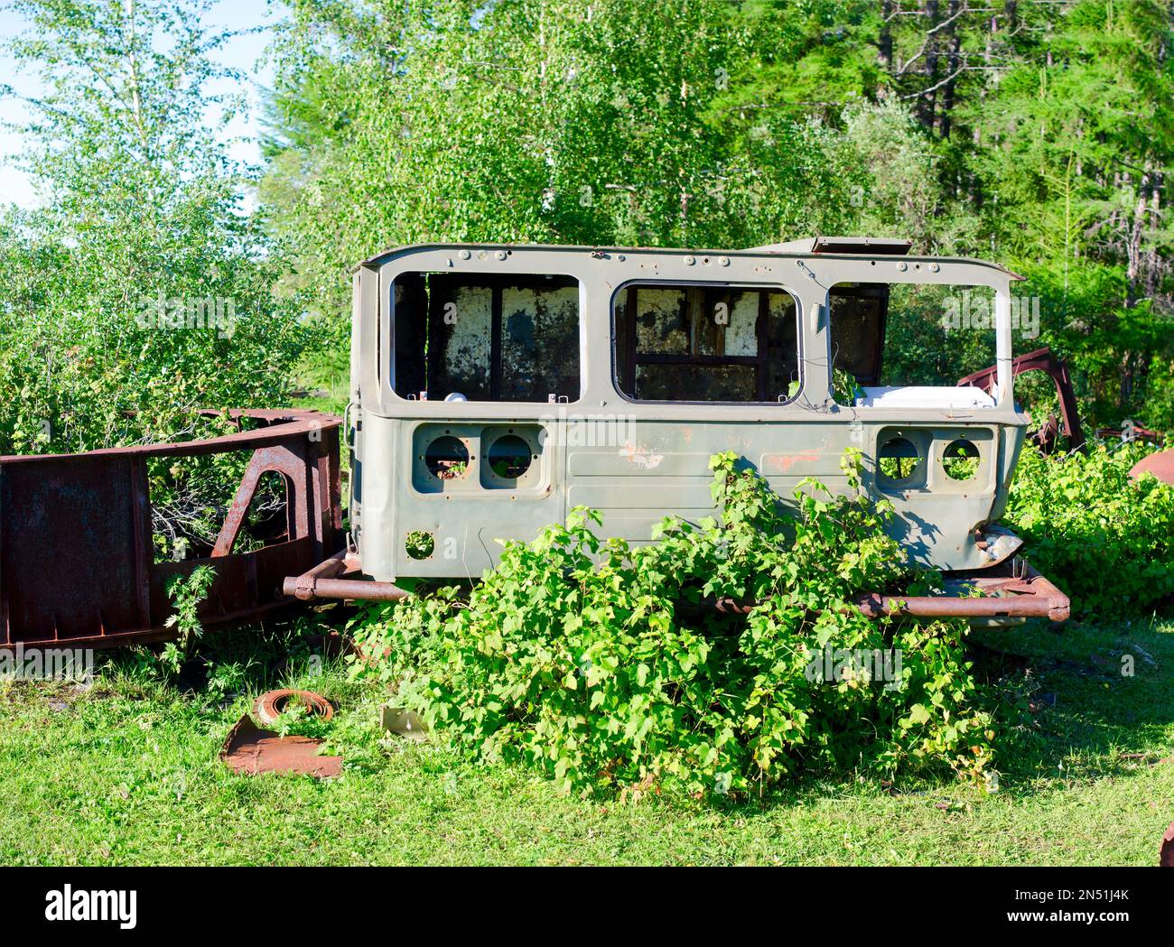 The old rusty body from the cabin of the Soviet car lies on the green grass in the field near the forest in the Northern taiga of Yakutia. Stock Photo