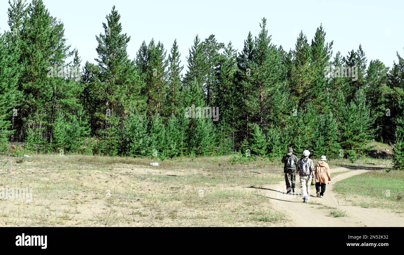 Yakut family of men with a woman and a young girl with a backpack is on the road going into the spruce forest. Stock Photo