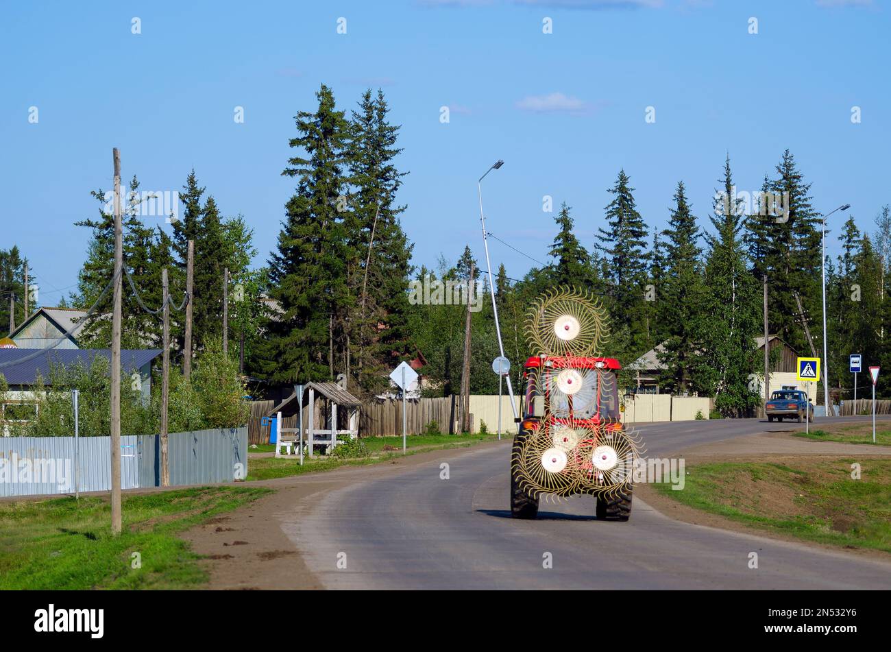 Tractor with a device for collecting hay rides on the road among the houses of the Northern village of Suntar in Yakutia. Stock Photo