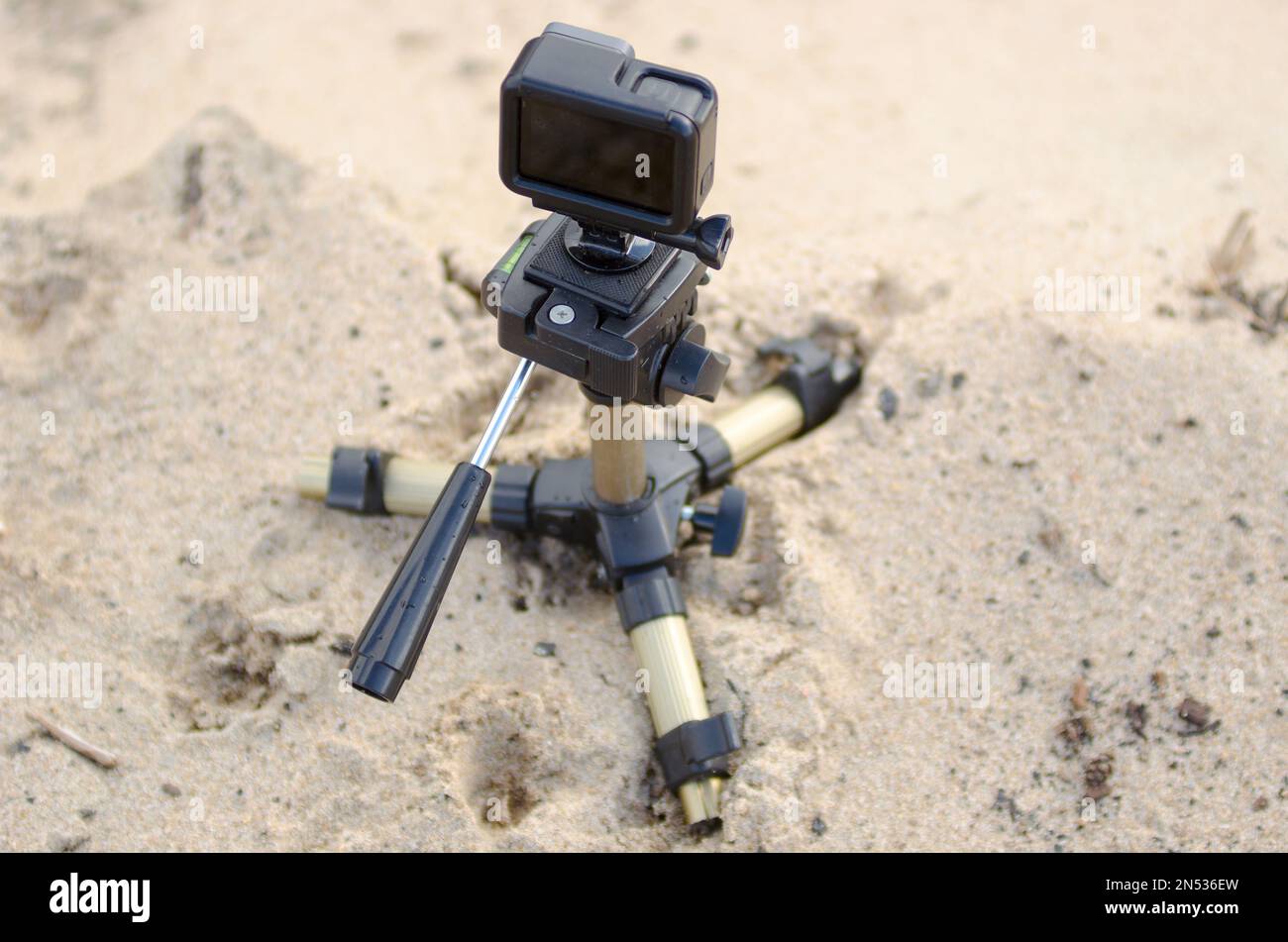 Action camera stands on a small tripod, recording video on a sandy beach. Stock Photo