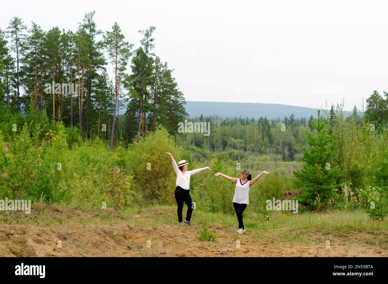 Yakut Asian girls pose with their hands up, standing on the slope of Homa against the background of the Northern taiga forest. Stock Photo