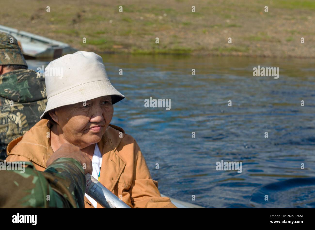 Sad adult Yakut woman in Panama looks at the river sitting in a boat with men on the brimstone. Stock Photo