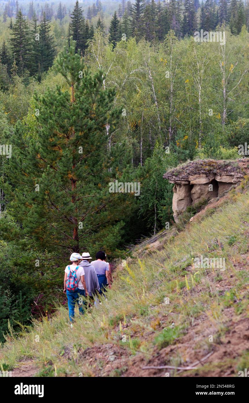 A group of Asian girls Yakut tourists with descend from the mountain past the attractions of erosive landforms, sandy mushrooms, in the Northern taiga Stock Photo