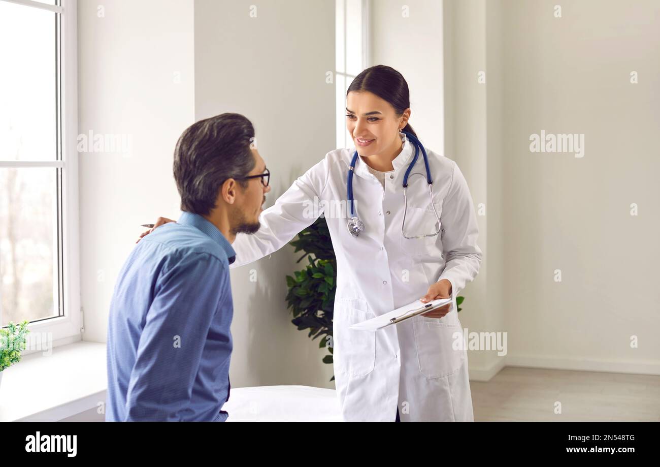 Professional female doctor approvingly, carefully puts her hand on the shoulder of young male patient. Stock Photo