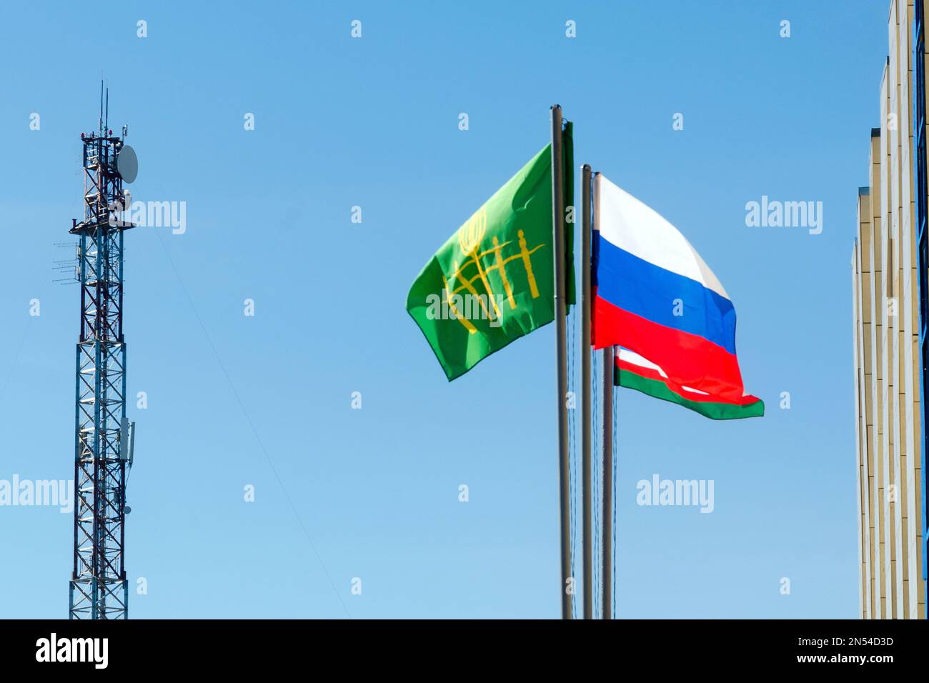 Three flags of Russia, Yakutia, and Suntara develop in the wind on the background of a radio tower near the administration building against the blue s Stock Photo