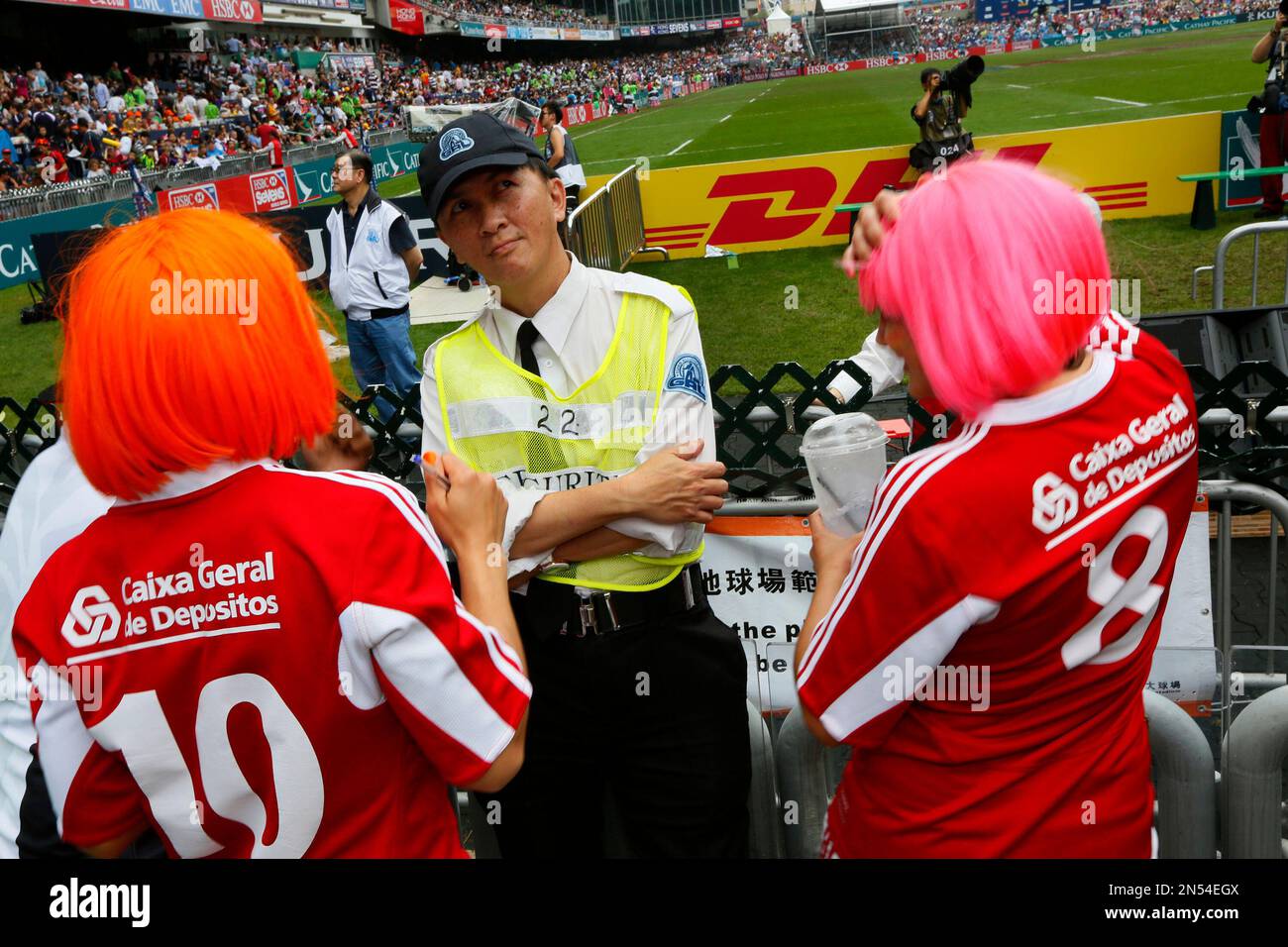 A security guard stands next to two rugby fans during the Hong Kong