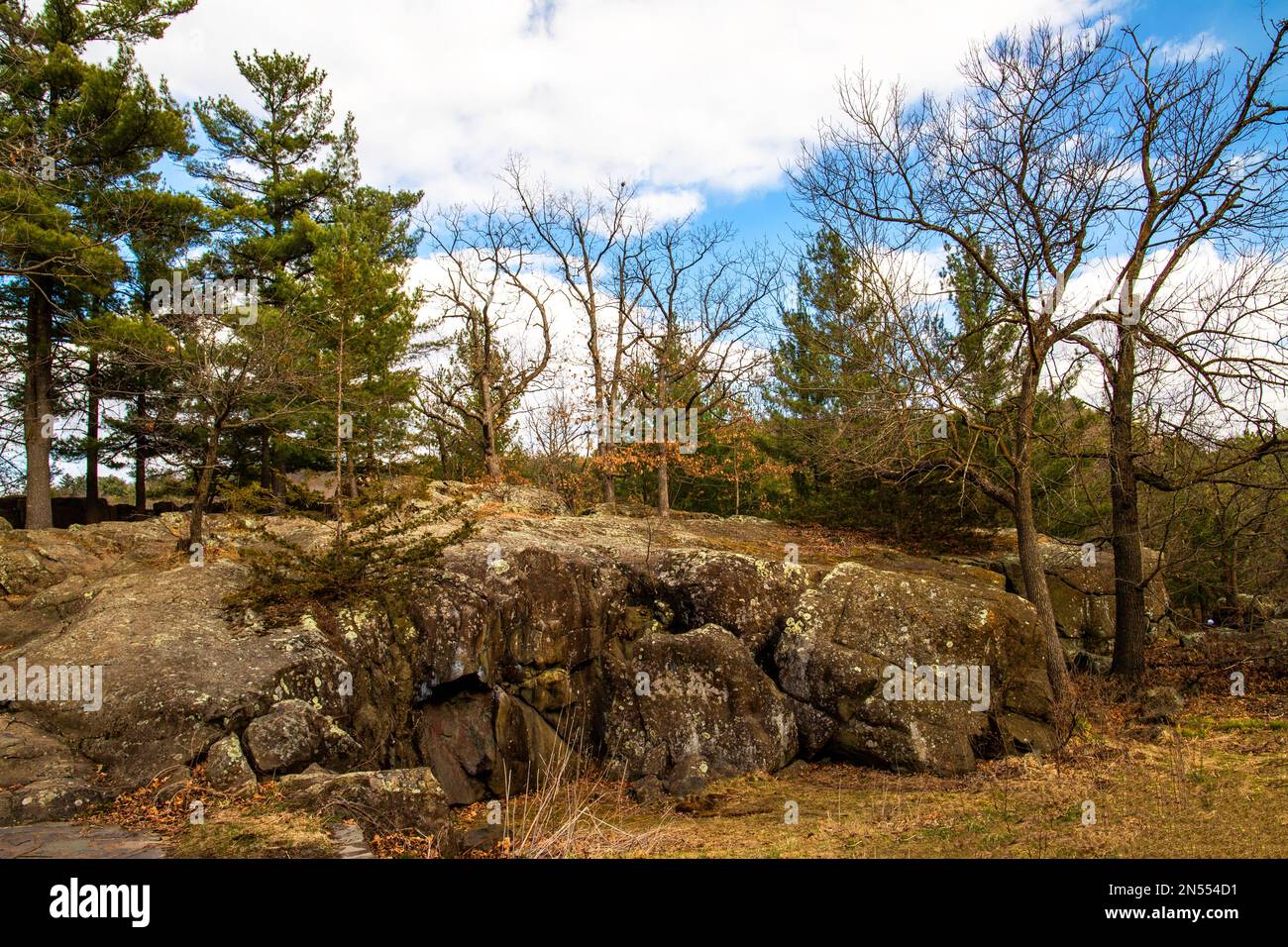 Basalt from the ancient lava flows make up the rock of Interstate State Park with trees against a cloudy blue sky in Taylors Falls, Minnesota USA. Stock Photo