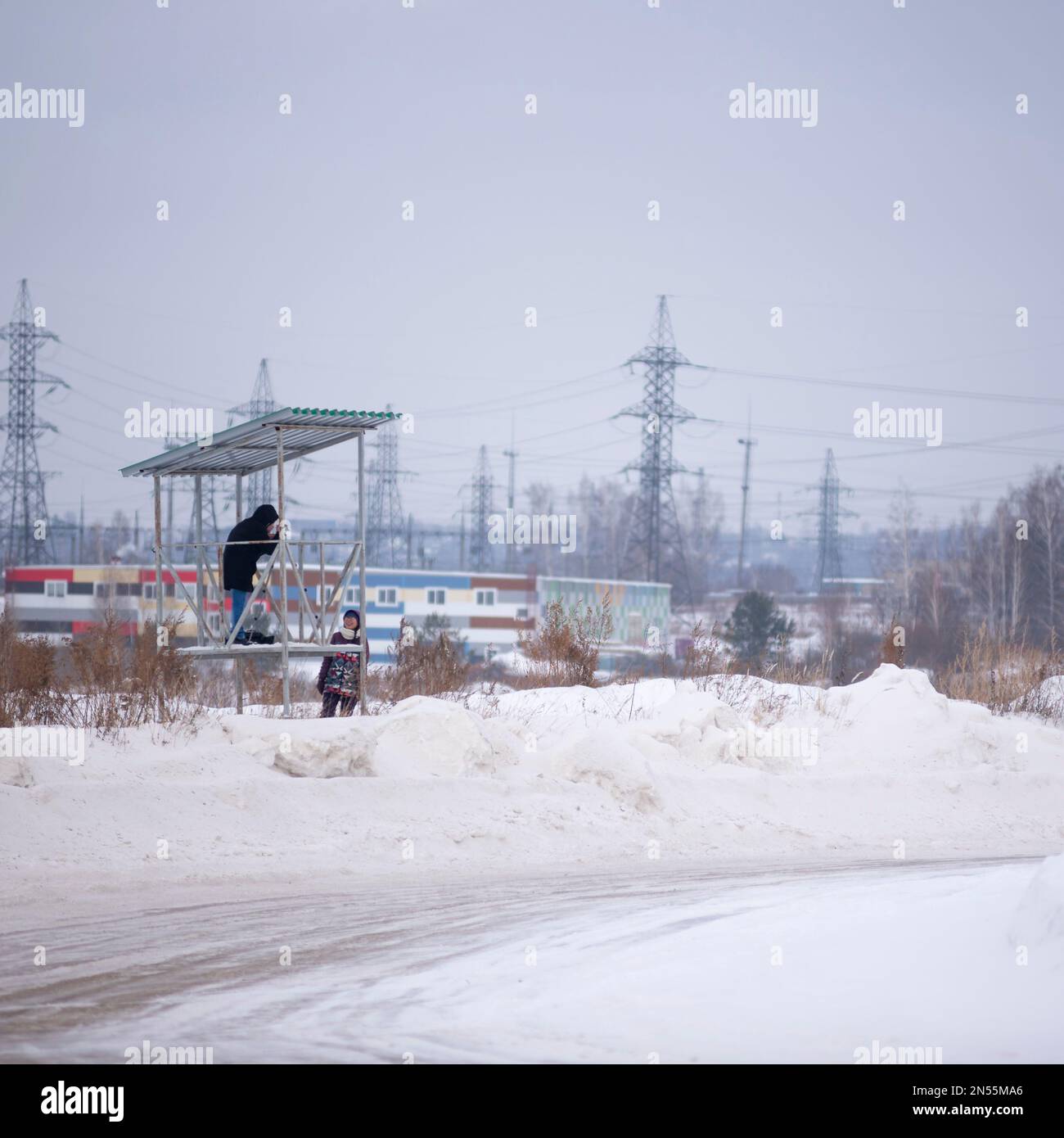 A photographer on a hill takes a picture of the road next to a smiling girl in winter from a tripod. Stock Photo