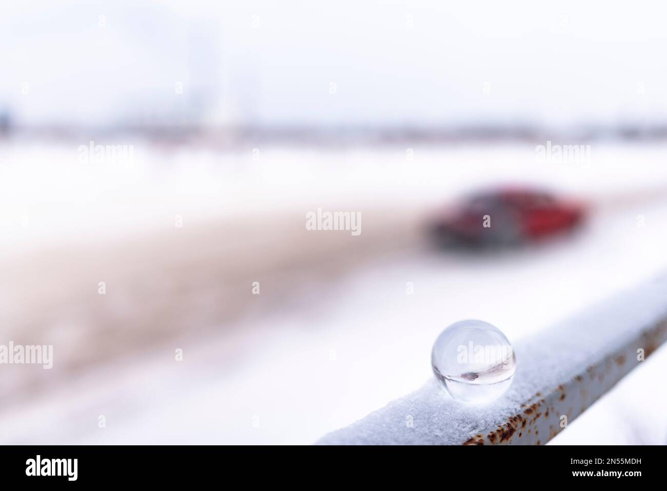 A round glass globe standing on a railing in the snow reflects the smeared silhouette of a passing car on the road in the city. Stock Photo