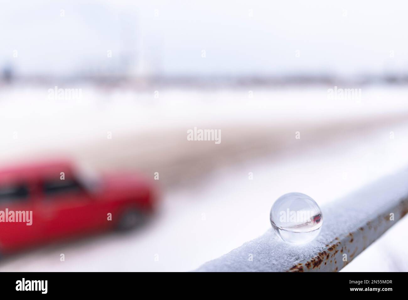 A round glass globe standing on a railing in the snow reflects the smeared silhouette of a passing car on the road. Stock Photo