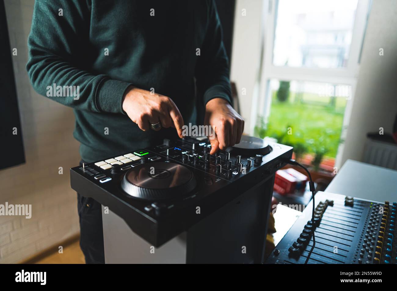 Hands of a man turning mixers and tapping on buttons on dj home set