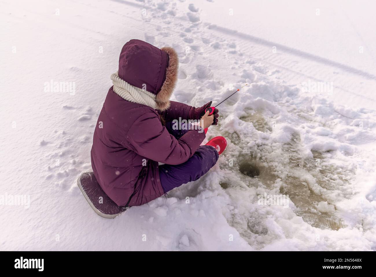 A lonely girl angler enthusiastically catches fish with a winter fishing rod sitting on a