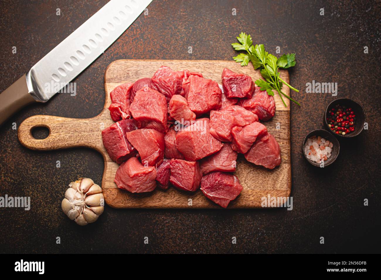 https://c8.alamy.com/comp/2N56DFB/raw-beef-meat-chopped-in-cubes-with-bunch-of-fresh-parsley-garlic-salt-and-pepper-on-wooden-cutting-board-with-knife-for-cooking-stew-or-meat-dish-2N56DFB.jpg