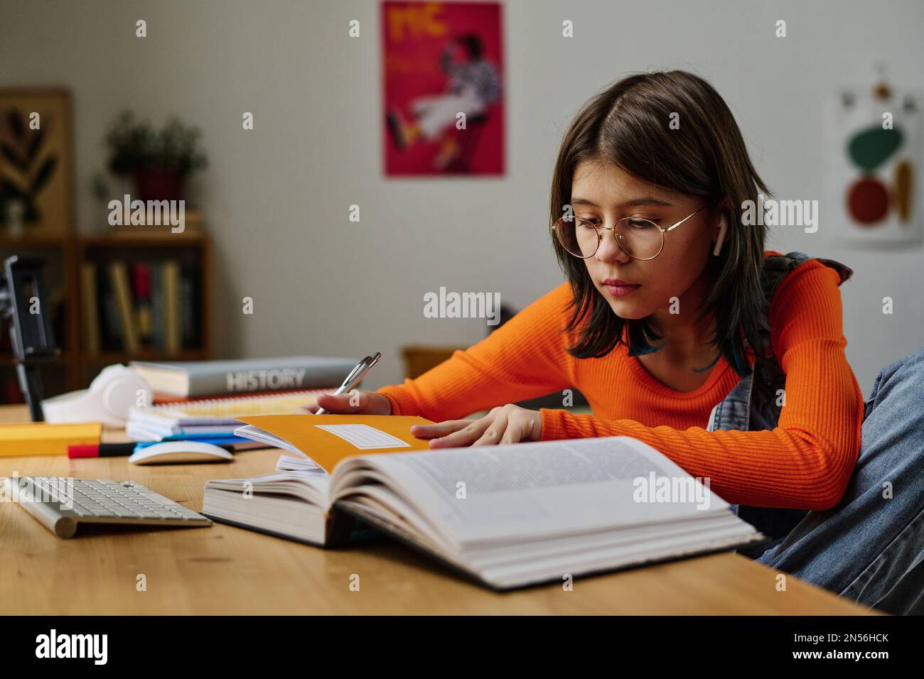 Teenage girl sitting at desk with books and notebooks and doing ...