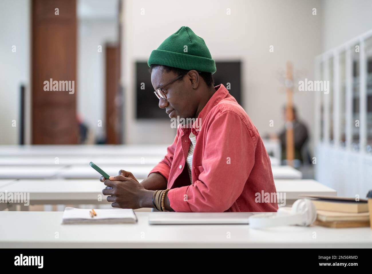 Smiling African guy student using smartphone during study break, sitting at desk in library Stock Photo