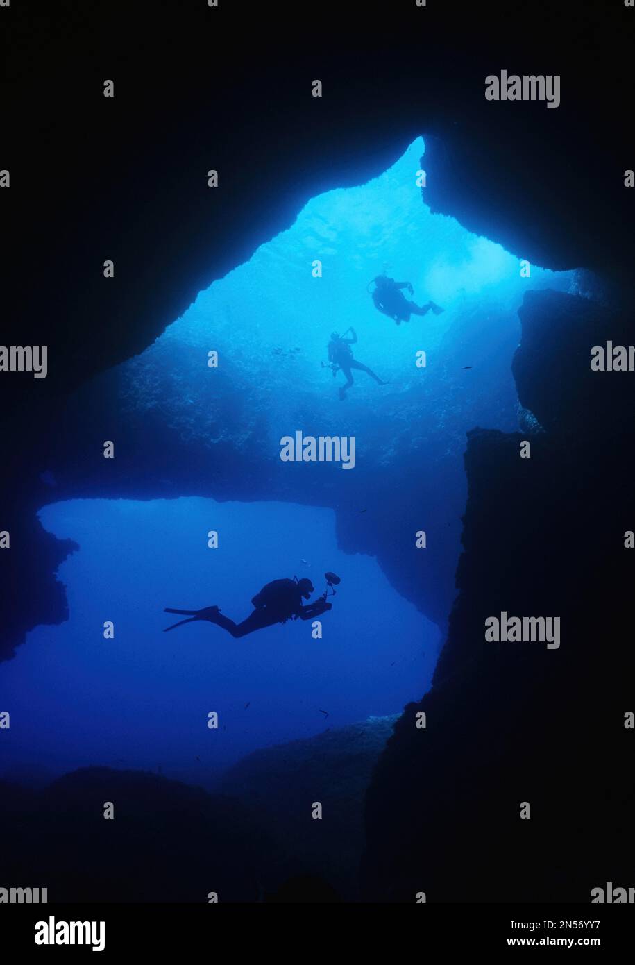 Diver underwater photographer swims dives through large underwater cave grotto Blue Dome Blue Hole on west coast of Gozo Island, Gozo, Malta Stock Photo