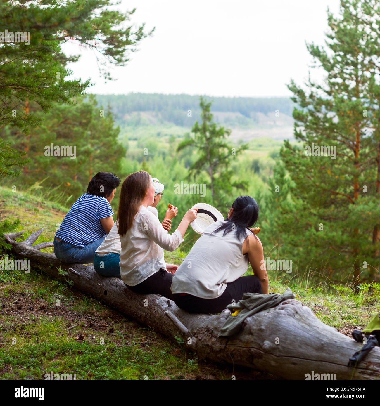 Four girls Yakut friends sitting on a log and communicate against the background of the wild North of the taiga and streams. Stock Photo
