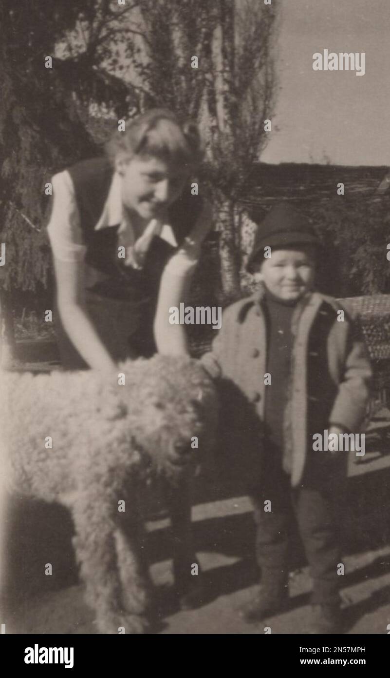 Vintage Photograph of Lady and her pet dog / hand holding puppy : Vintage family photo mom with little boy standing with them loving big white curly shepherd dog. Happy smiling family photo from the 1930s. little caress dog Stock Photo