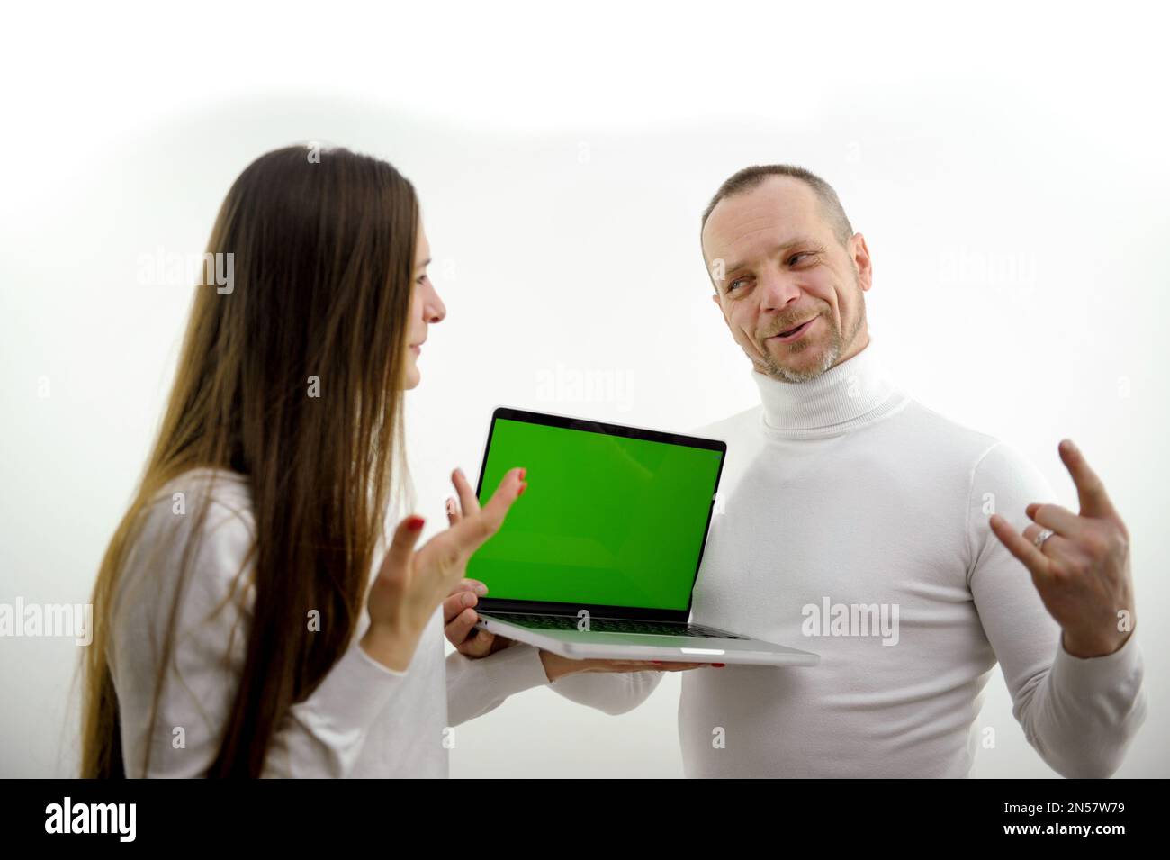 man and girl near laptop with green screen chromakey dressed white background man tells to student teacher she listens to new information online learning interest entertainment communication Stock Photo