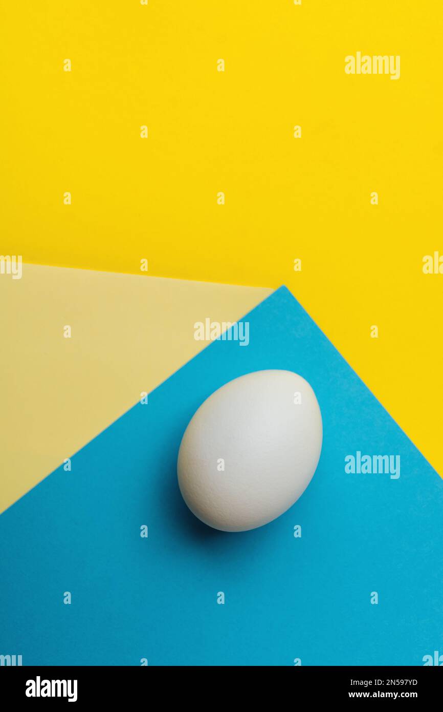 White egg on abstracts yellow and blue geometric paper background. The concept of Ukrainian refugees in search of safety and love for Ukraine. Copy sp Stock Photo