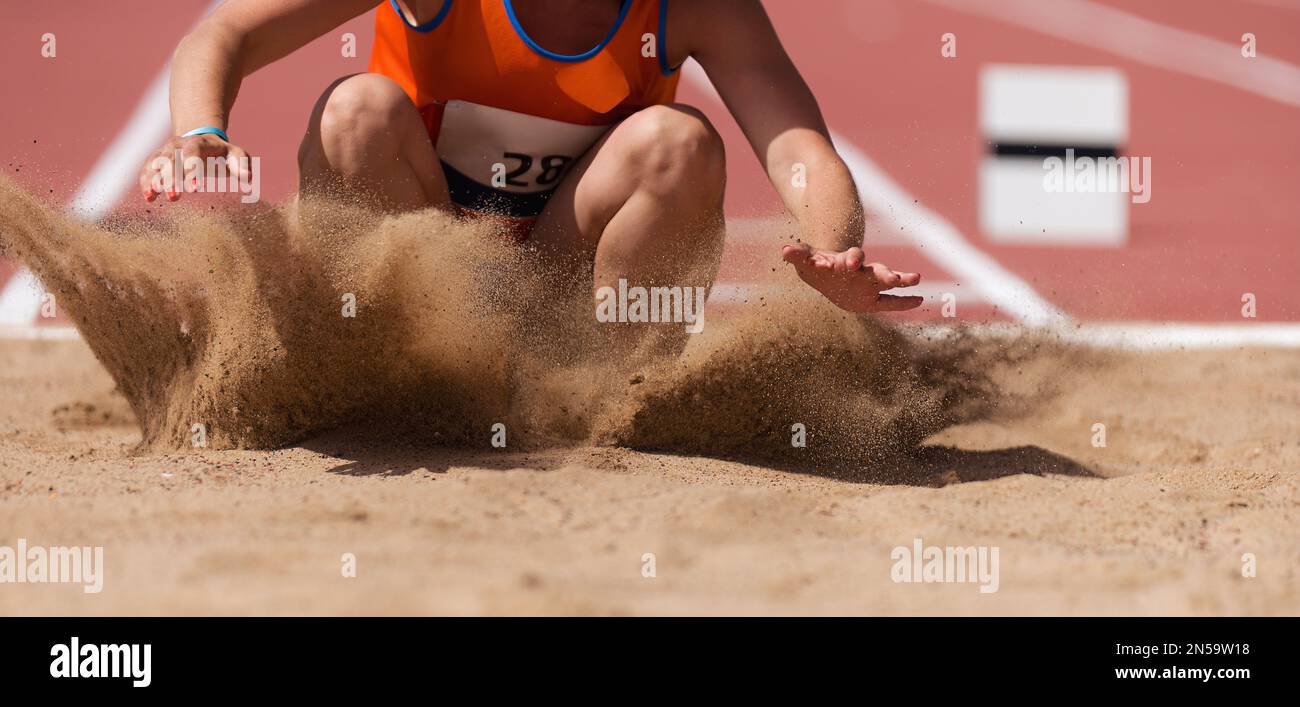 Female athlete long jump landing sand spray, landing in long jump in