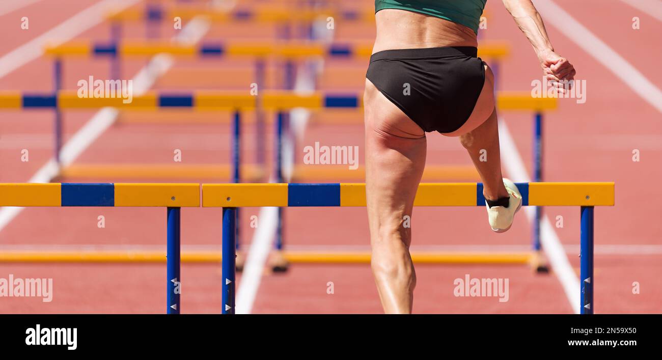 Athlete running a hurdle race in a stadium, runner jumping over an