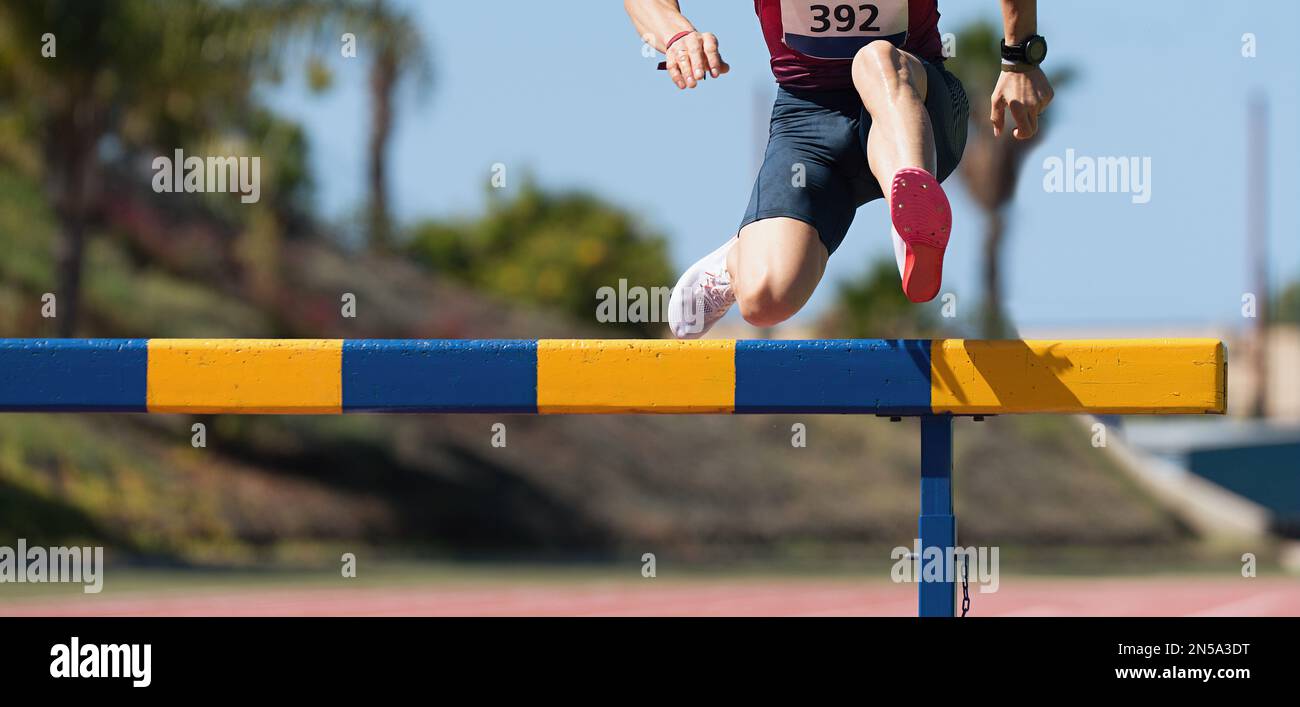 Athlete running a hurdle race in a stadium, runner jumping over a hurdle during track and field
