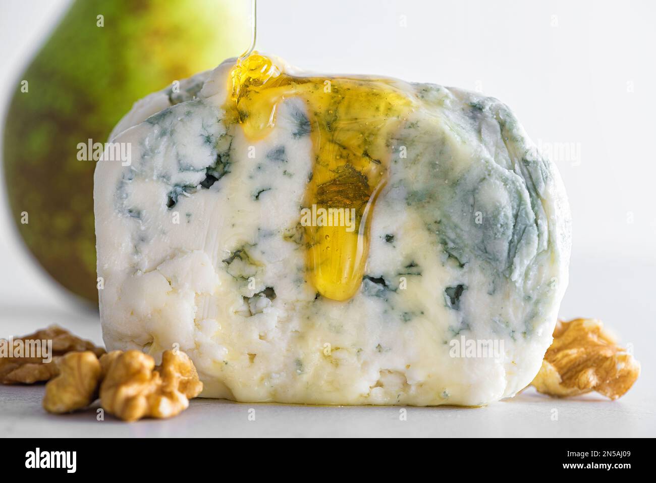 Pouring honey on blue cheese dorblu or gorgonzola with pear and walnuts on white background. Close up. Tasty food Stock Photo