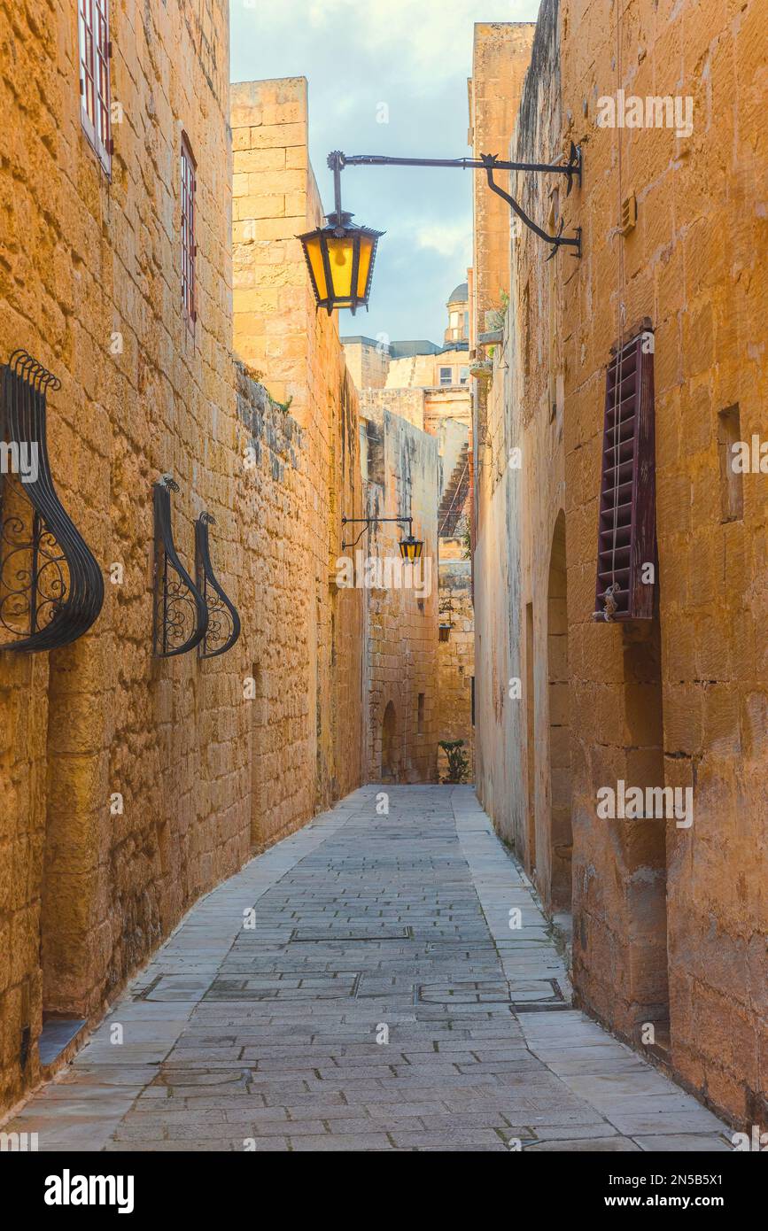 Empty narrow medieval ancient street with street lights in Mdina town ...