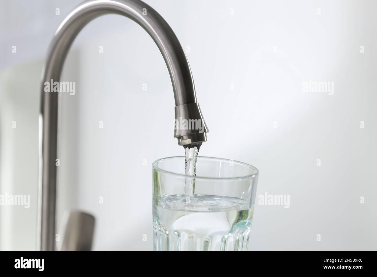 Filling glass with clear water from faucet on light background, closeup Stock Photo