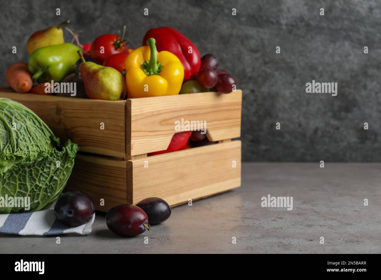 Wooden crate full of different vegetables and fruits on grey table ...