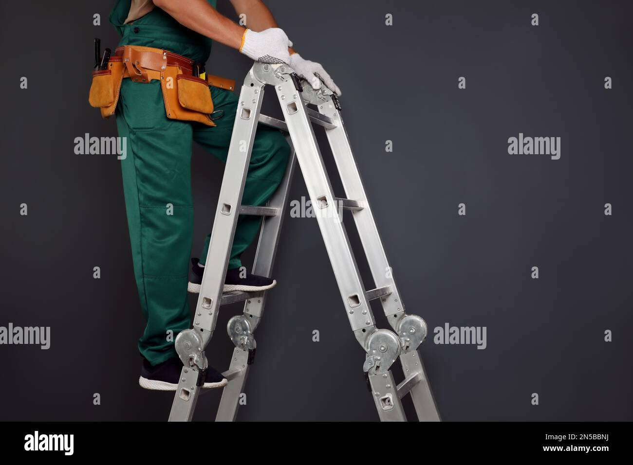 Professional constructor climbing ladder on black  background, closeup Stock Photo