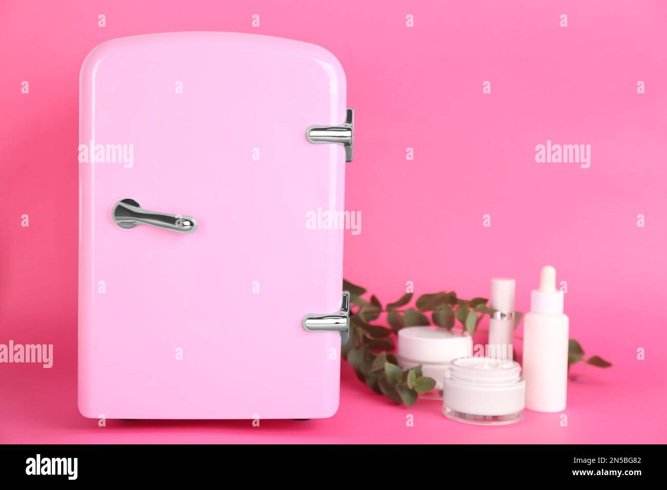 Cosmetic refrigerator and skin care products on pink background Stock