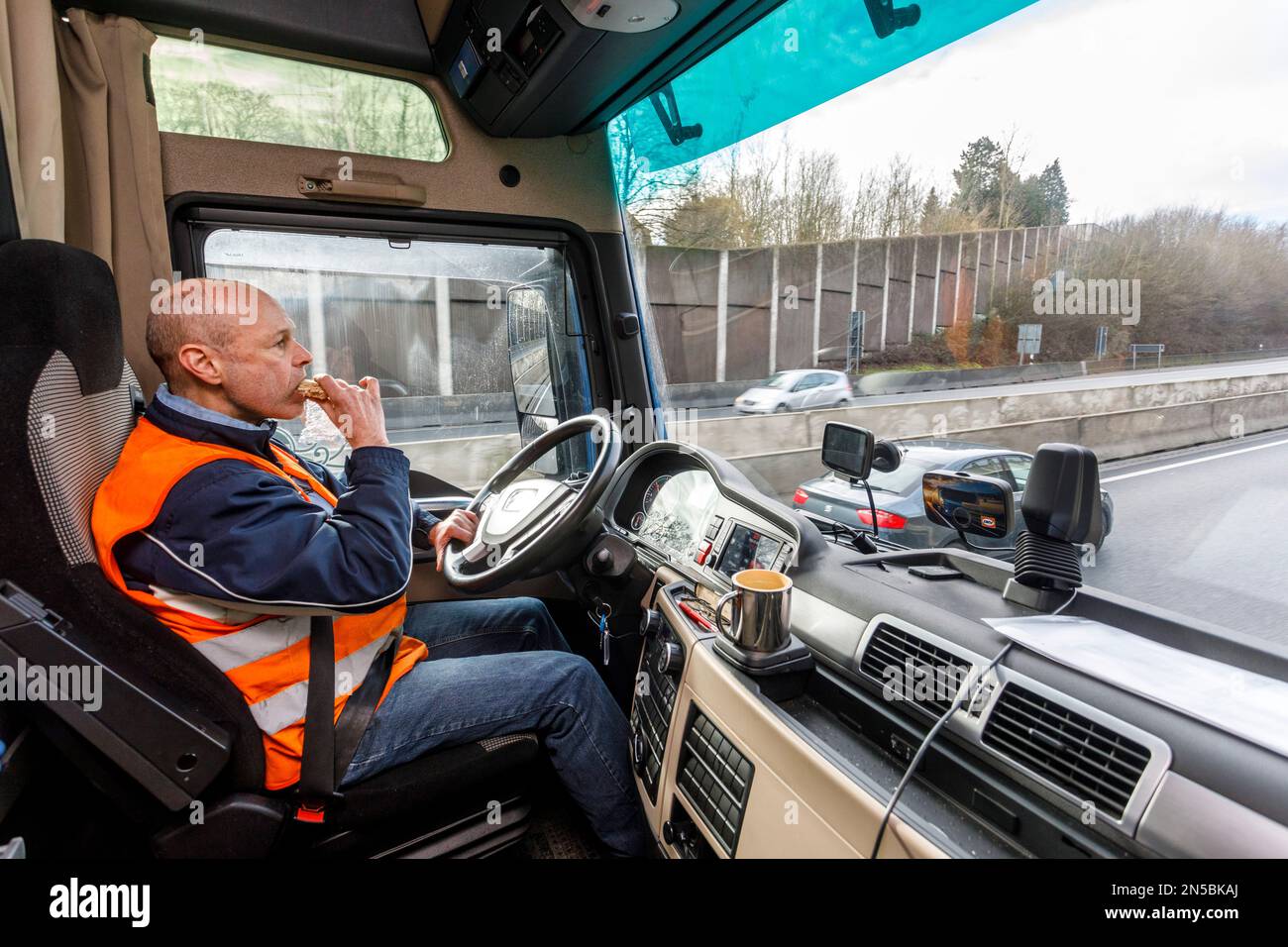 Professional long-distance drivers on the Autobahn, having breakfast in the driver's cab behind the wheel Stock Photo