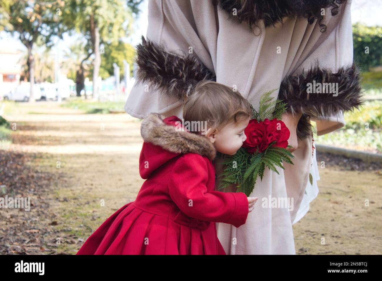 A cute little white Caucasian girl smelling a bouquet of roses held by her mother Stock Photo