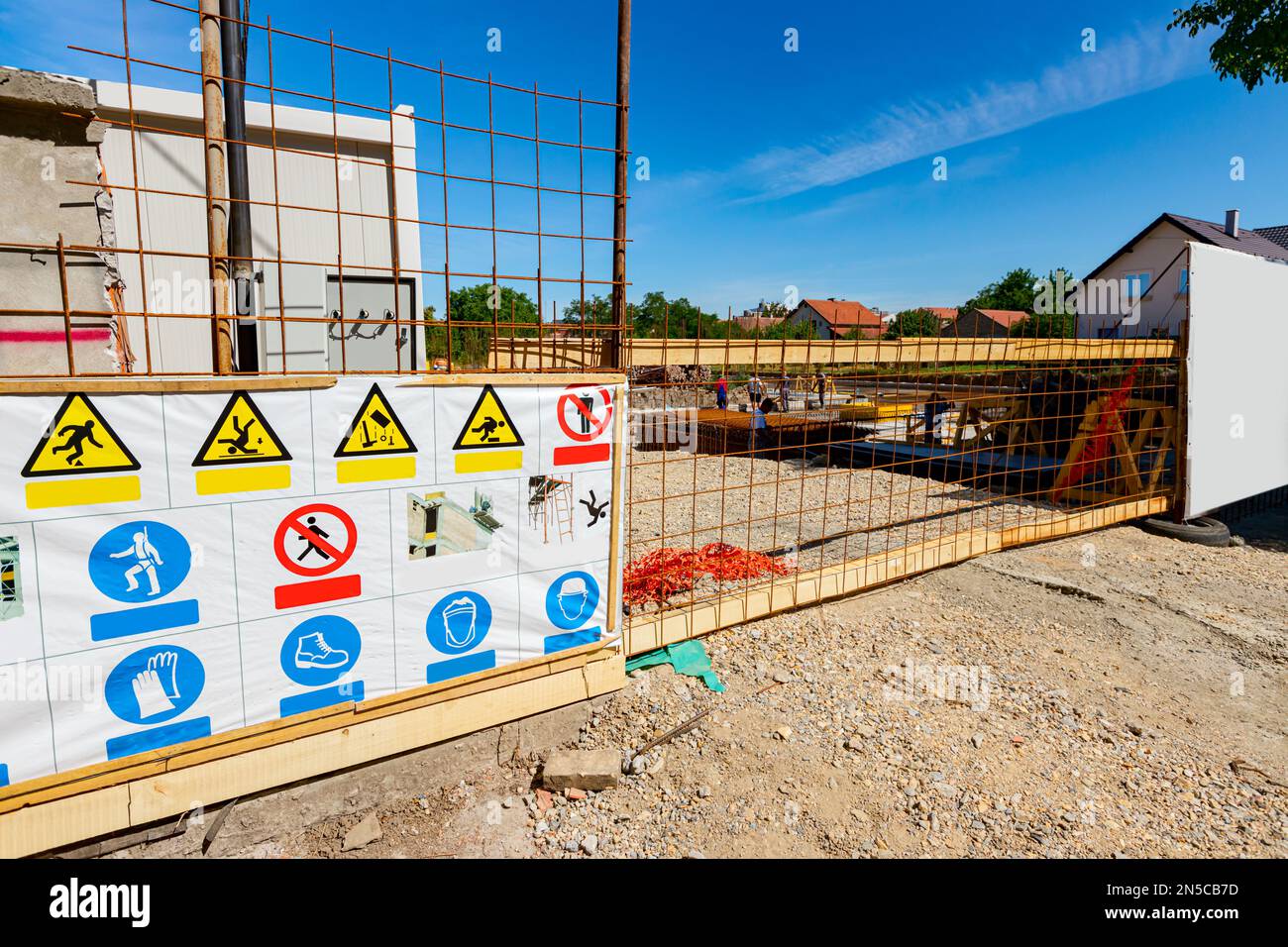 Board with safety regulations is standing in front fenced edifice under construction. Entrance, gate made of square reinforcement, on building site, r Stock Photo